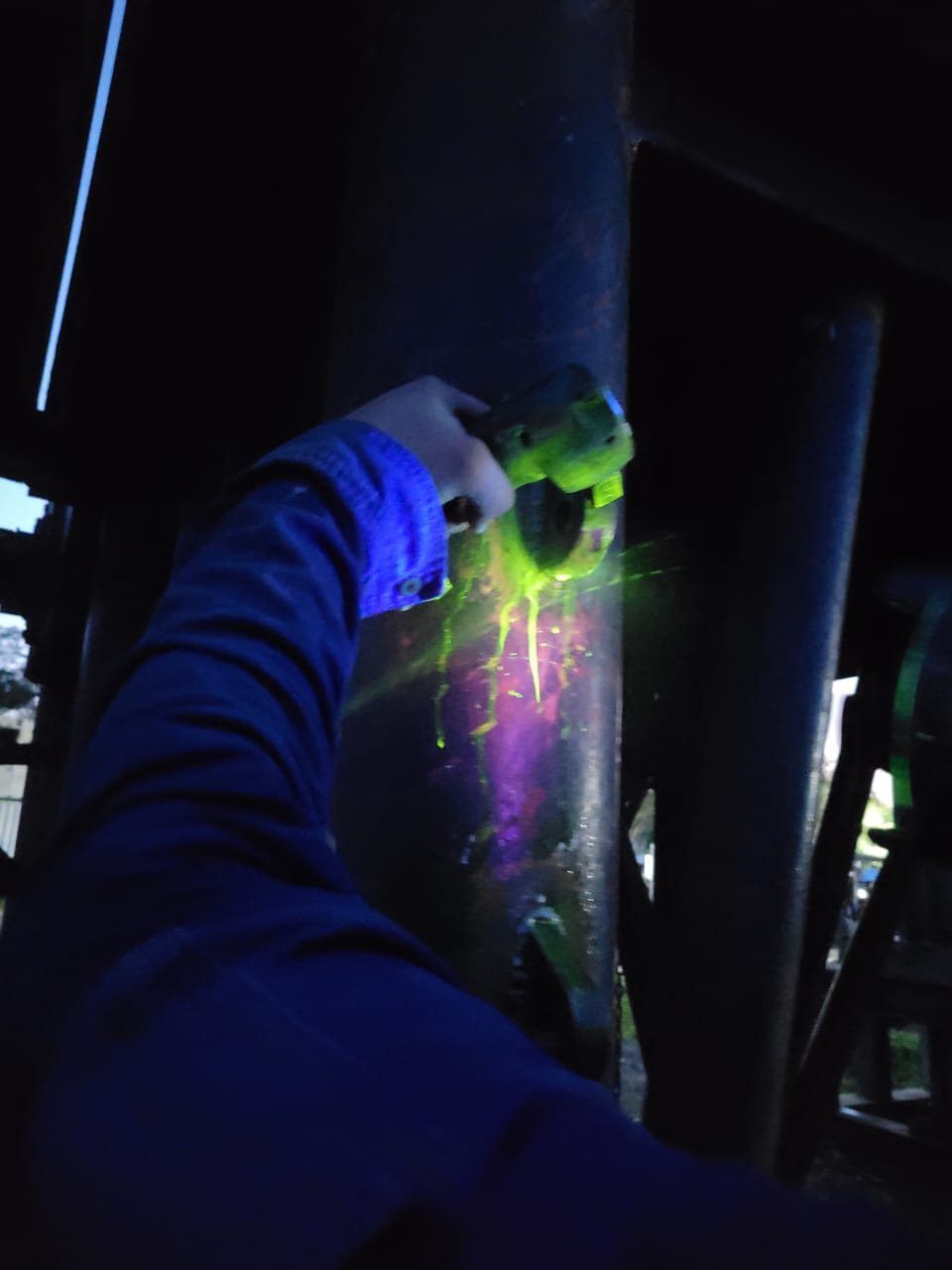 Técnico aplicando lámpara de luz ultravioleta sobre un tubular durante una inspección nocturna en campo